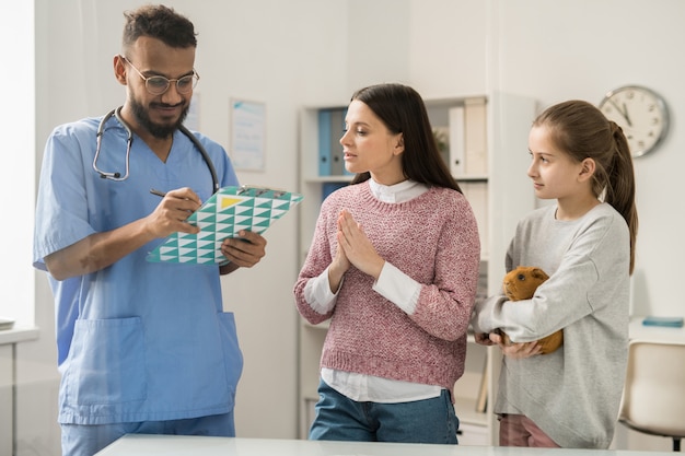 Jovem médico veterinário fazendo prescrições médicas para cobaias e conversando com os proprietários de animais de estimação