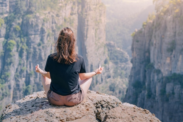 Jovem meditando em pose de ioga de lótus no topo do penhasco com vista para a vista panorâmica do desfiladeiro Tazi na Turquia