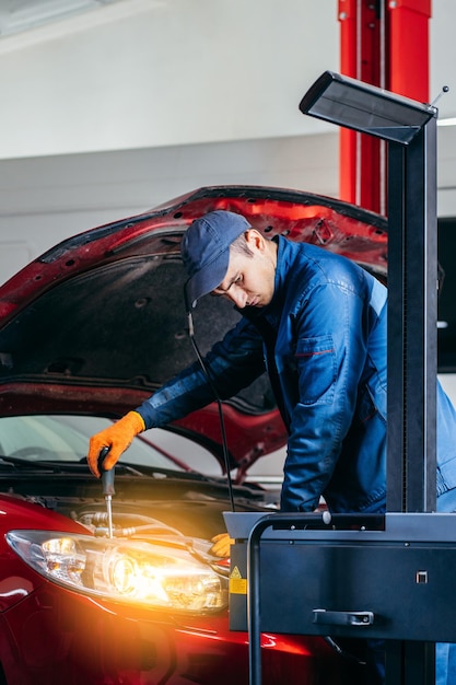 Foto jovem mekânico ajustando os faróis do carro moderno vermelho em serviço automático