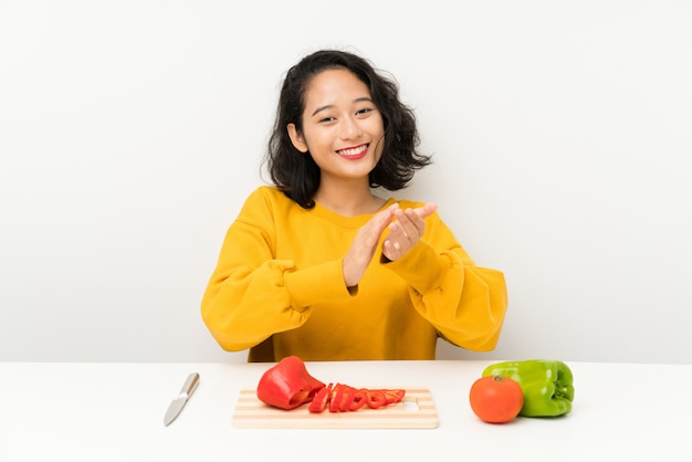 Jovem menina asiática com legumes em uma mesa aplaudindo