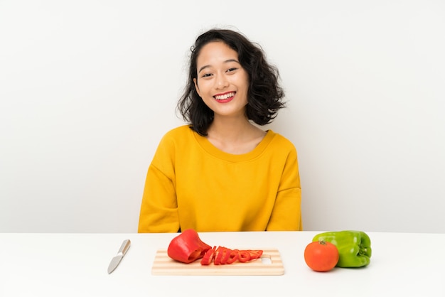Jovem menina asiática com legumes em uma mesa com expressão facial de surpresa