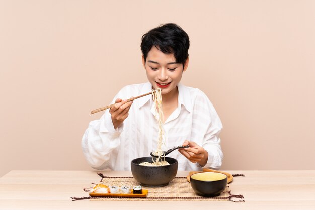 Jovem menina asiática em uma mesa com uma tigela de macarrão e sushi