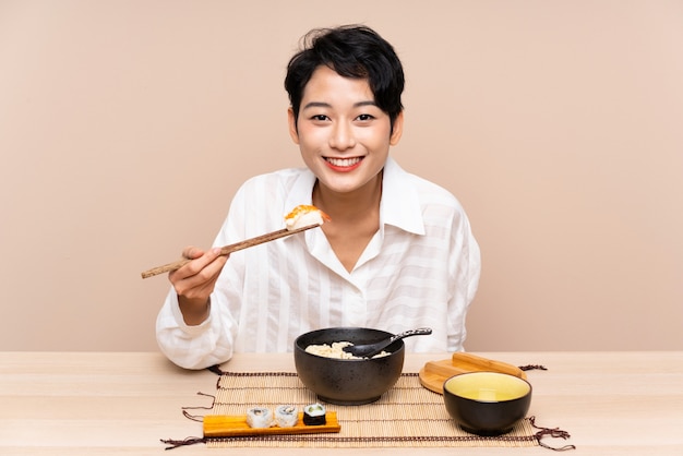 Jovem menina asiática em uma mesa com uma tigela de macarrão e sushi