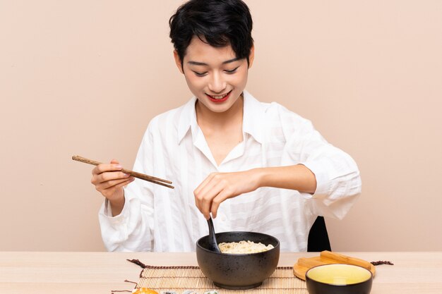 Jovem menina asiática em uma mesa com uma tigela de macarrão e sushi