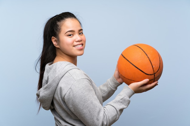 Jovem menina asiática jogando basquete na parede isolada