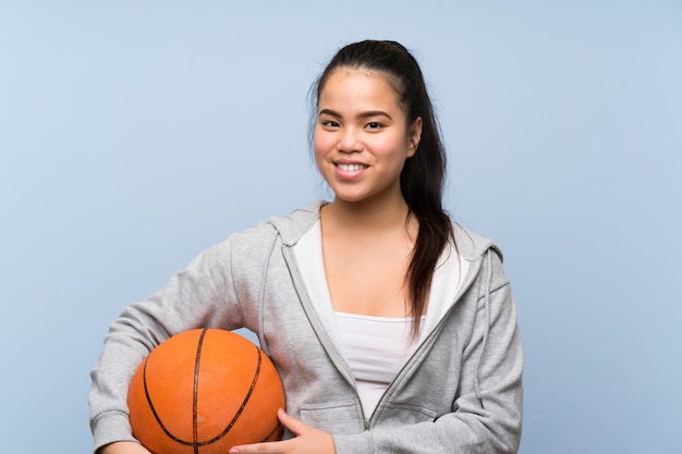 Jovem menina asiática jogando basquete na parede isolada