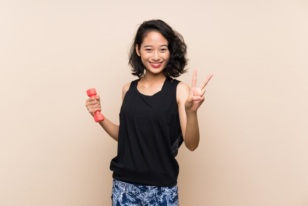 Jovem, menina asiática, levantamento halterofilismo, isolado, parede, sorrindo, e, mostrando, sinal vitória