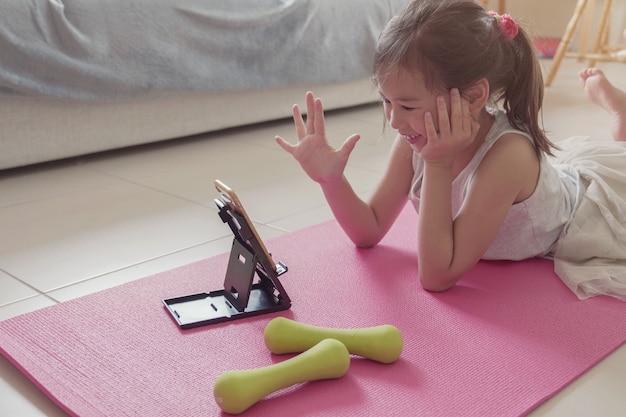 Jovem menina asiática mista assistindo streaming de vídeos no laptop, treino de treino em casa, zoom aula de exercícios on-line, conceito de distanciamento social