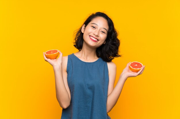 Jovem menina asiática segurando uma toranja sobre parede laranja isolada