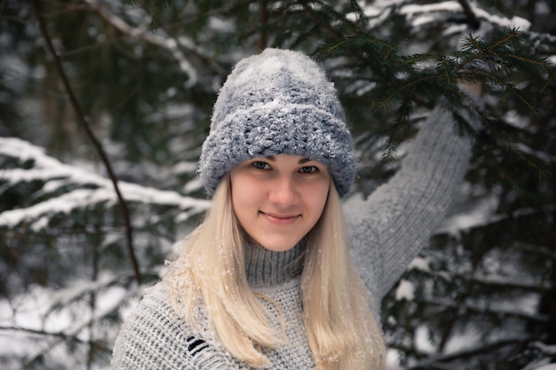 Jovem menina bonita com cabelo branco comprido joga bolas de neve. Ela se diverte, joga neve e se alegra com a queda de neve. Caminhada de inverno lá fora.