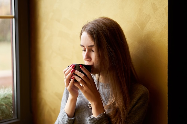 Jovem menina bonita com cabelos longos, bebendo café ou chá no café.