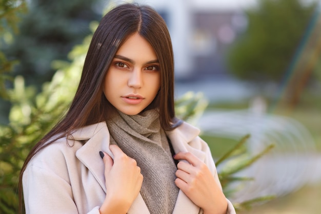 Jovem menina bonita e elegante com longos cabelos escuros caminhando ao ar livre no casaco cinza ao pôr do sol