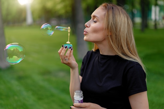 Jovem menina bonita infla bolhas de sabão no parque ensolarado de verão