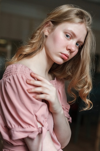 Jovem menina bonita loira de olhos azuis no vestido rosa, inclinando a cabeça.