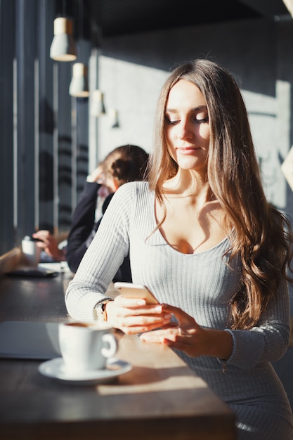 Jovem menina bonita no café usa um smartphone