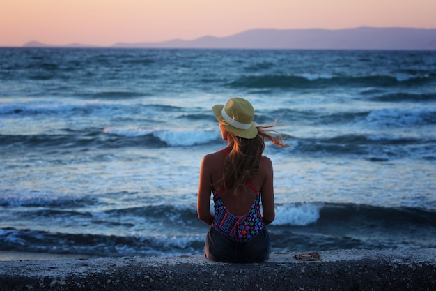 Foto jovem menina bonita sentada perto do mar, o pôr do sol no verão