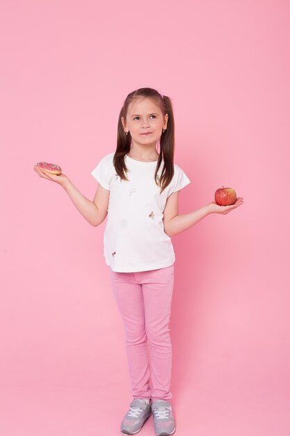 Jovem menina com estrondo segurando a maçã vermelha e donut alegremente.