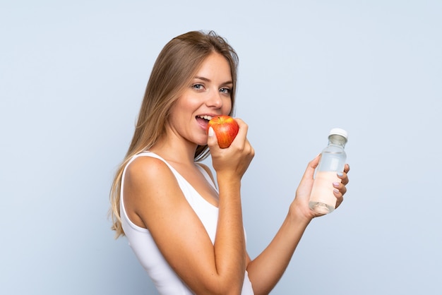 Jovem menina loira com uma maçã e uma garrafa de água sobre o fundo isolado