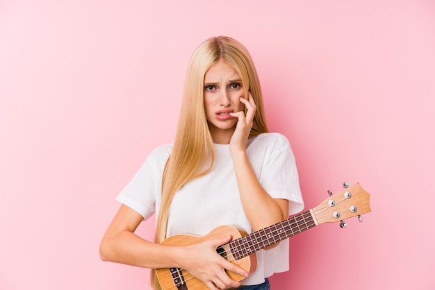 Jovem menina loira tocando ukelele roer unhas, nervoso e muito ansioso.