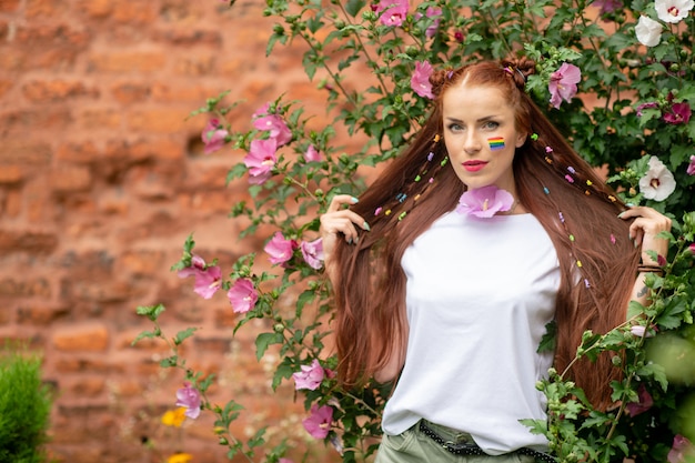 Jovem menina morena cabelos longos bonita com arco-íris lgbt no rosto, posando em flores desabrochando