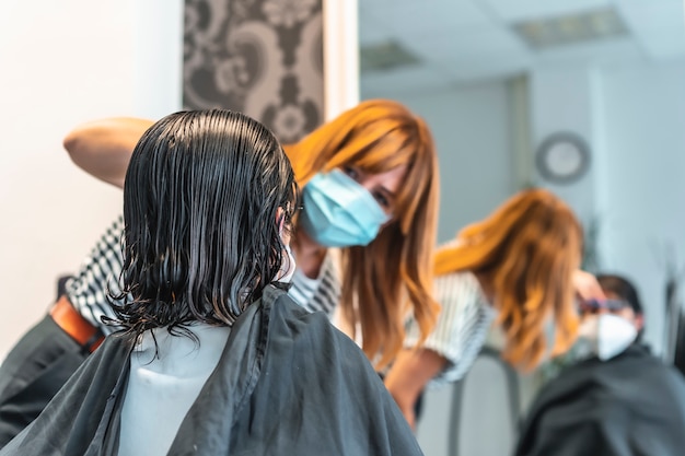 Jovem menina morena com máscara em um cabeleireiro cortando o cabelo refletido no espelho. medidas de segurança para cabeleireiros na pandemia de covid-19. novo normal, coronavírus, distância social