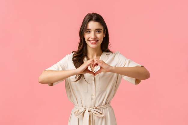 Jovem menina morena de vestido, mostrando sinal de coração