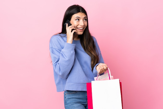 Jovem menina morena isolada rosa segurando sacolas de compras e chamando um amigo com seu telefone celular