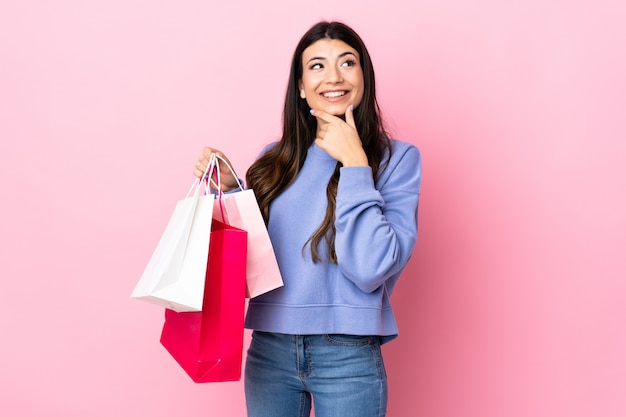 Jovem menina morena isolada rosa segurando sacolas de compras e pensando