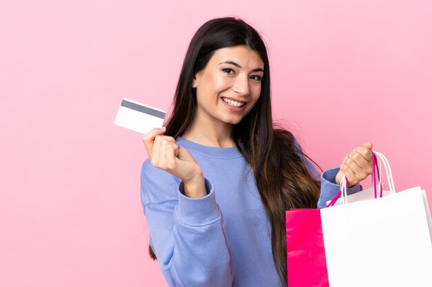 Jovem menina morena parede rosa segurando sacolas de compras e cartão de crédito