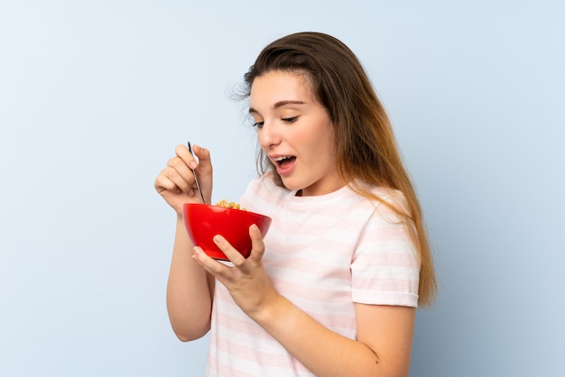 Jovem menina morena segurando uma tigela de cereais sobre parede isolada