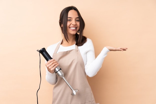 Jovem menina morena usando um liquidificador manual sobre um fundo isolado, segurando o imaginário de copyspace na palma da mão para inserir um anúncio