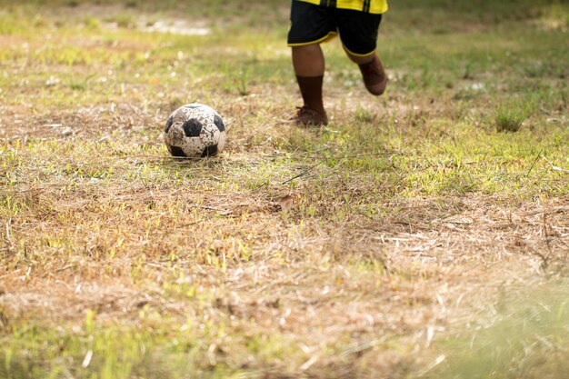 Jovem menino asiático jogando futebol no campo