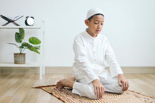 Jovem menino muçulmano orando em tapete de oração e fazendo um gesto de movimento no procedimento de salat