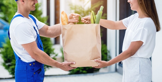 Jovem mensageiro entregando mercadorias para uma jovem em casa.