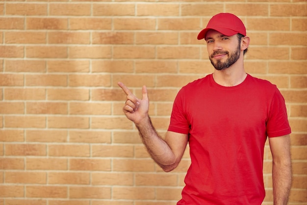 Jovem mensageiro masculino caucasiano alegre em uniforme vermelho