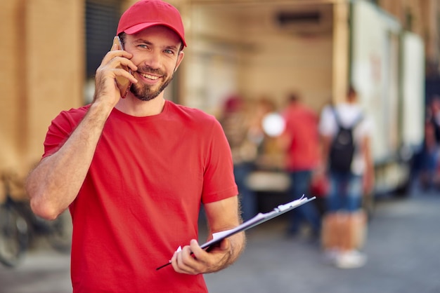 Foto jovem mensageiro masculino caucasiano falando ao telefone no pátio do armazém