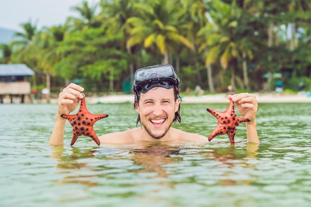 Jovem mergulhador feliz segurando estrela do mar, sorrindo, olhando para a câmera