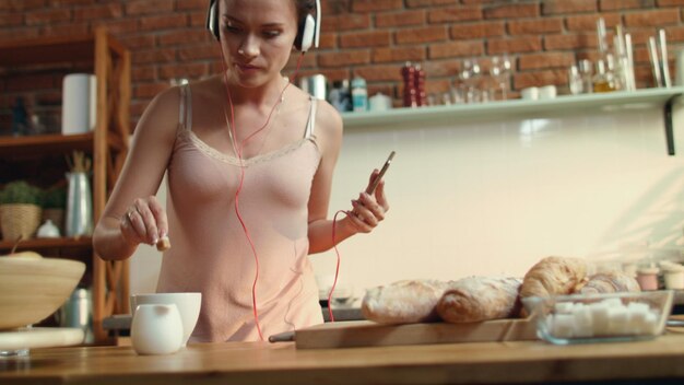 Jovem mergulhando açúcar no café Dançarina ouvindo música na cozinha