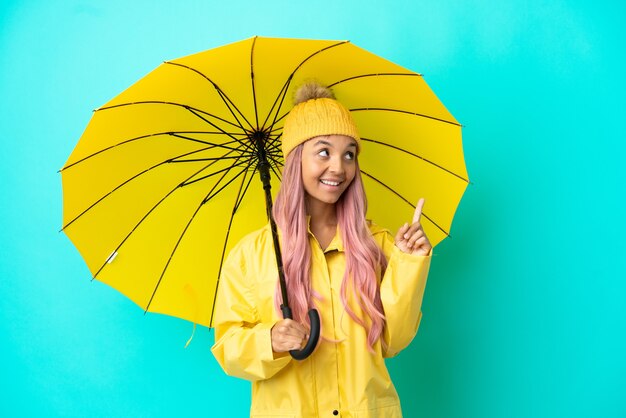 Jovem mestiça com casaco à prova de chuva e guarda-chuva apontando uma ótima ideia