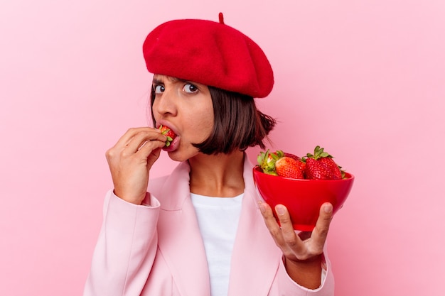 Jovem mestiça comendo morango isolado em parede rosa