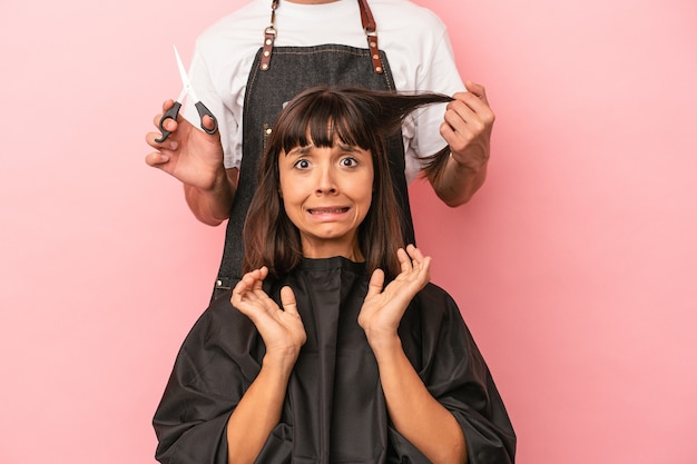 Jovem mestiça cortando o cabelo no cabeleireiro isolado em fundo rosa