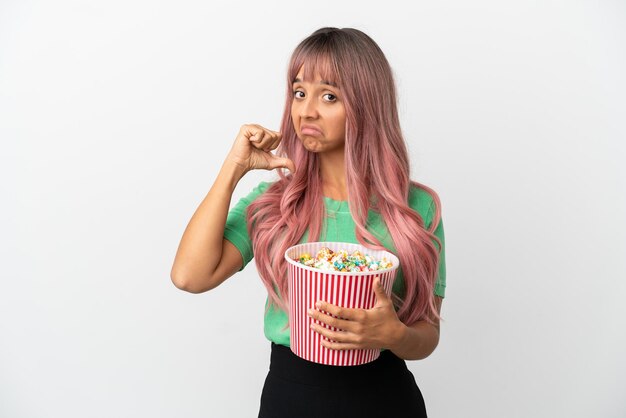 Jovem mestiça de cabelo rosa comendo pipoca isolada no fundo branco, orgulhosa e satisfeita