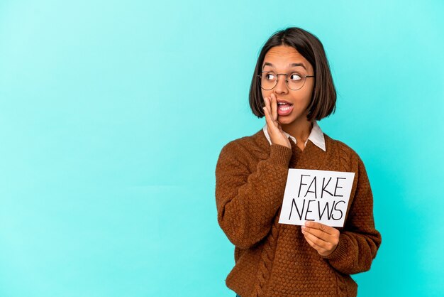 Jovem mestiça hispânica segurando um cartaz de notícias falsas está contando uma notícia secreta de travagem e olhando para o lado