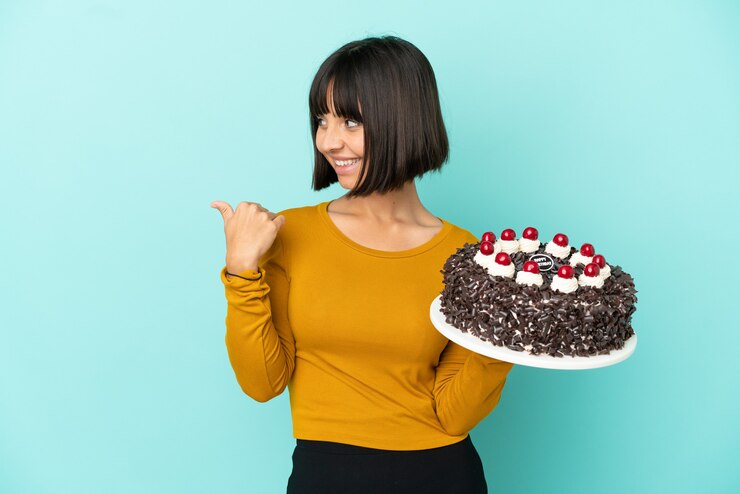 Foto jovem mestiça segurando bolo de aniversário apontando para o lado para apresentar um produto