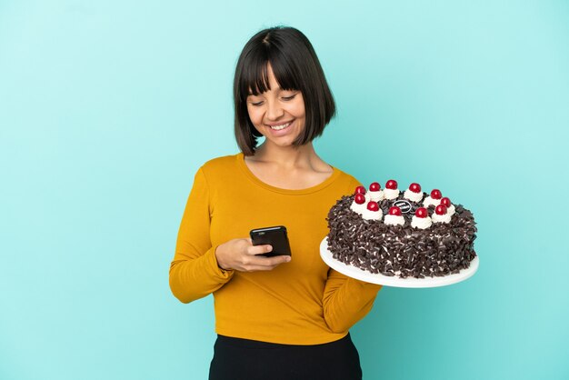 Jovem mestiça segurando bolo de aniversário enviando mensagem com o celular