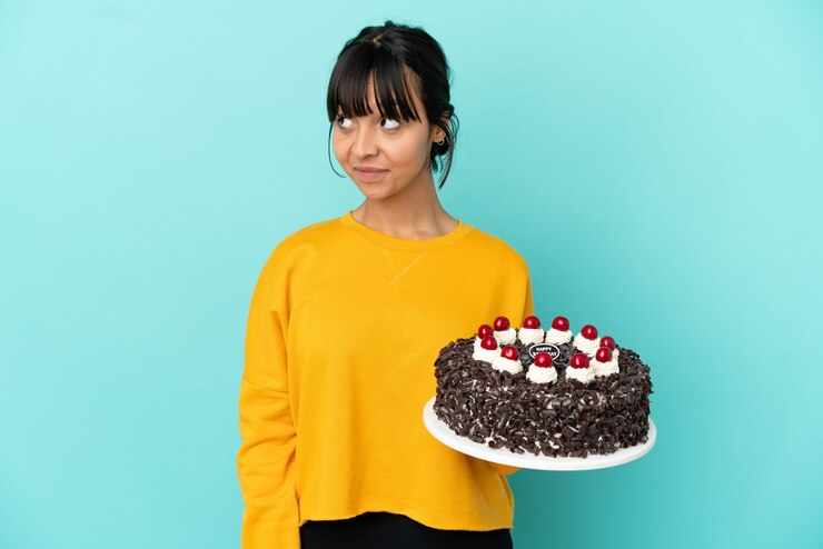 Foto jovem mestiça segurando um bolo de aniversário com dúvidas enquanto olha de lado