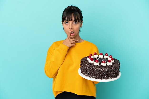 Jovem mestiça segurando um bolo de aniversário surpresa e chocada ao olhar para a direita