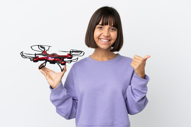 Jovem mestiça segurando um drone isolado no fundo branco apontando para o lado para apresentar um produto