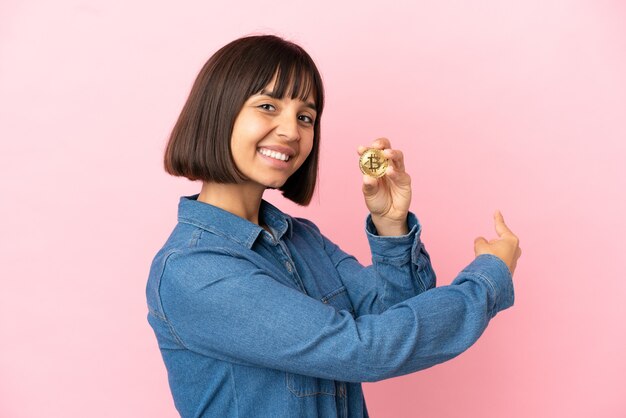 Foto jovem mestiça segurando um fundo isolado de bitcoin apontando para trás