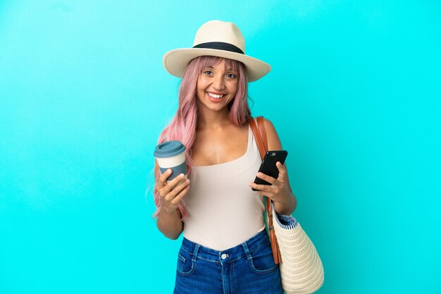 Jovem mestiça segurando uma bolsa de praia com Pamela isolada em um fundo azul segurando um café para levar e um celular